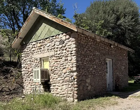 A small stone building with a gabled roof and an air conditioner unit mounted in a window.