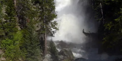 A large waterfall surrounded by evergreen trees and rocky terrain.