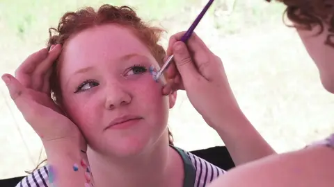 A person having their face painted with a brush.