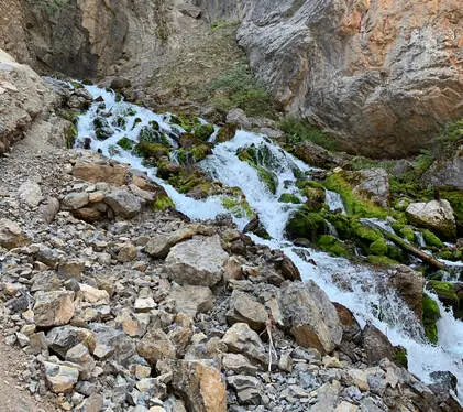 A small cascading stream flows over mossy rocks between rocky mountain slopes.