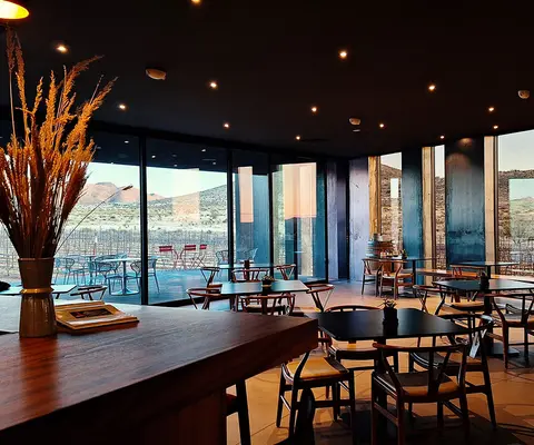 An interior view of a modern restaurant with large windows overlooking a landscape and vineyards.