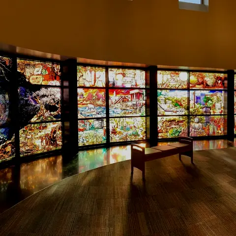 An interior view of a room with large stained glass windows and a bench on the floor.