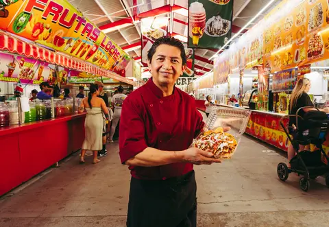 A man in a red uniform holds a container of food inside a bustling market.