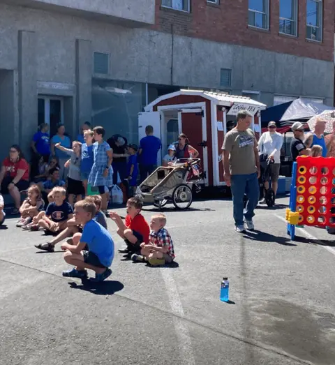 A crowd of people and children gather on a street during an outdoor event.