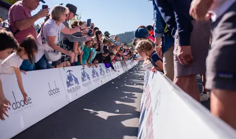 A crowd of spectators watches a ball race along a fenced track outdoors.