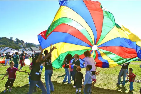 A group of people playing with a colorful parachute outside on a grassy field.
