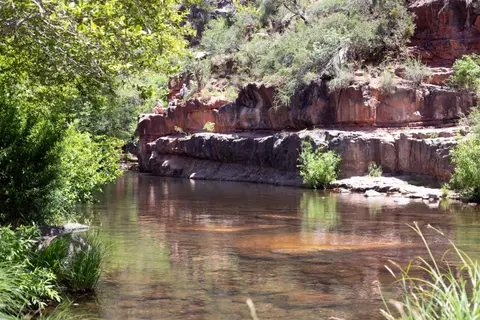 A scenic river flowing past rocky cliffs and green vegetation.