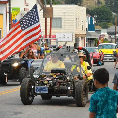 People drive vehicles in a parade down a street.