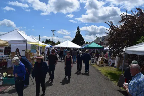 People walking through an outdoor market with white tents under a cloudy sky.