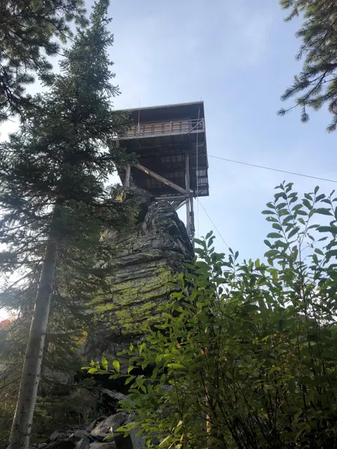 A wooden lookout tower is built on top of a rocky outcrop surrounded by trees.