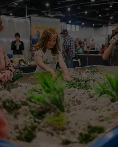 A young girl plays with a sand table at an indoor event.