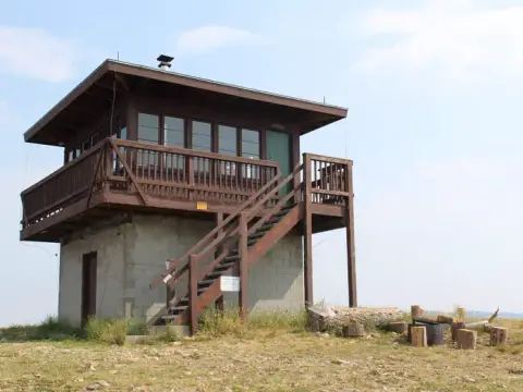 A fire lookout tower stands outdoors on a grassy hilltop.