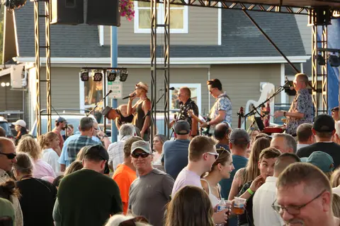 A band performs on an outdoor stage before a crowd of people.