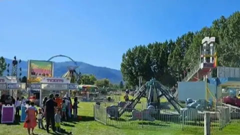 A photo shows an outdoor carnival with rides and booths on a grassy field.