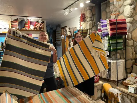 Two women hold up woven blankets inside a shop.