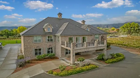 An exterior view of a large two-story stone building with a dark tiled roof and a balcony overlooking a driveway.