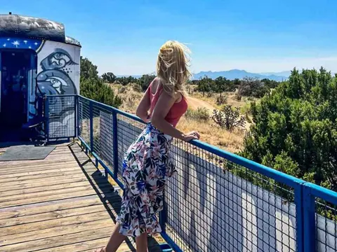 A woman stands on a wooden deck overlooking a landscape.