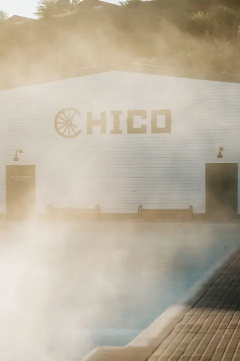 Steam rising from an outdoor pool in front of a white building.