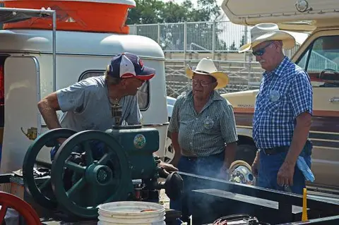 Three men examine an old engine outdoors.