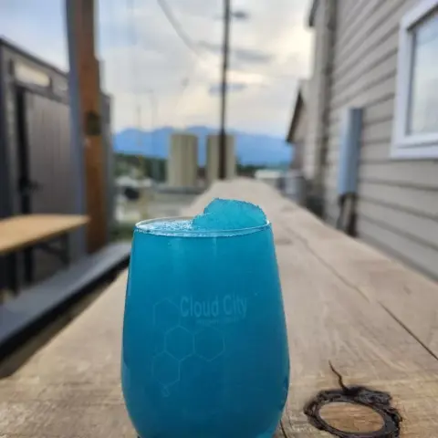 A blue beverage in a glass sits on a wooden counter outdoors.