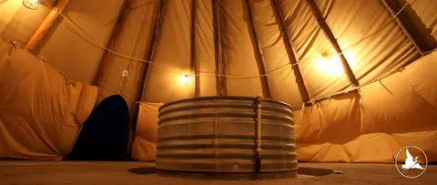 An interior view of a large tent with a metal stock tank in the center.