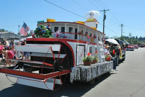 A decorated paddleboat float is pulled down a street during a parade.