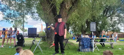 A street performer in a top hat and vest performs outdoors in front of a tree.