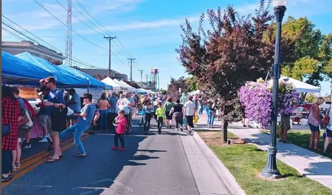 A street market with vendors and shoppers on a sunny day.