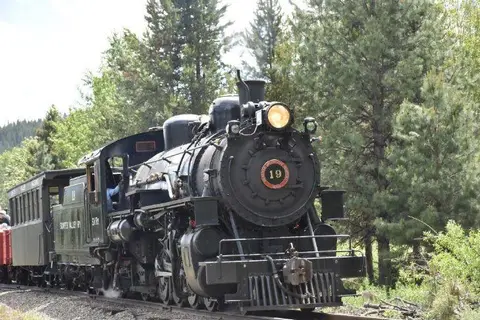 A vintage steam train travels along a track past trees.