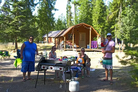 A group of people gathered outside a log cabin at a campsite.
