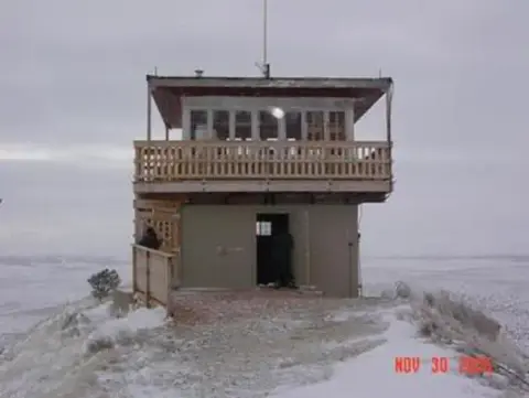 A fire lookout tower stands on a snow-covered hill.