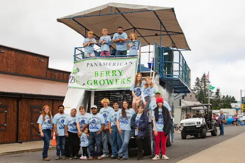 A group of people pose in front of a large berry harvesting machine with a banner.