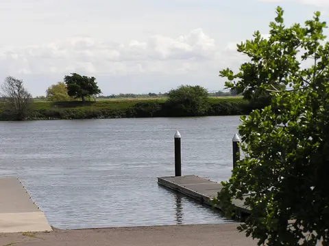 A boat ramp extends into a wide river under a cloudy sky.