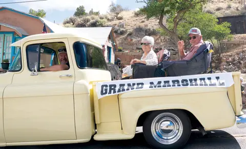 A vintage pickup truck labeled Grand Marshall carries people down a street.