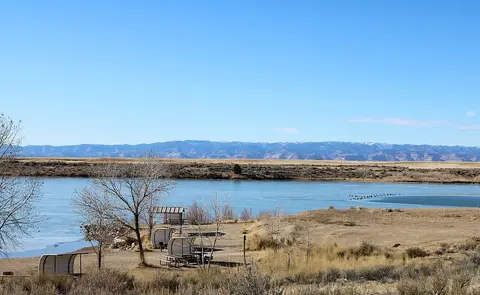 A scenic view of a lake with distant mountains under a blue sky.