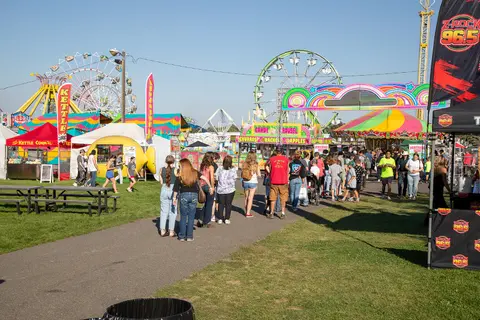 People walking along a path at a carnival with rides in the background.