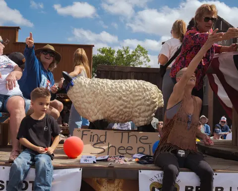 A group of people riding on a parade float featuring a large model sheep.
