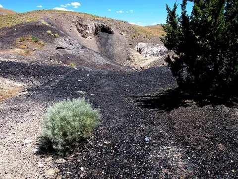 A landscape view showing dark volcanic terrain with sparse vegetation and a clear blue sky.