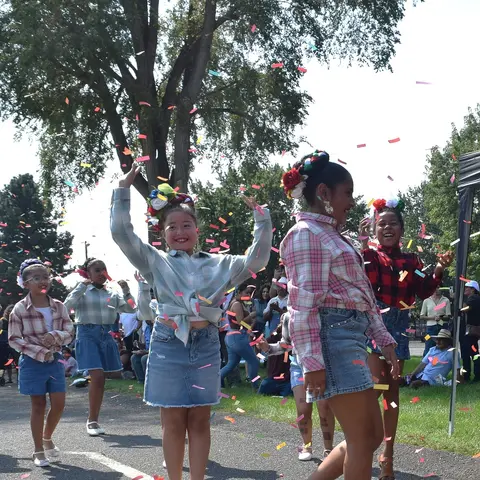 A group of young people celebrate outdoors with confetti falling around them.