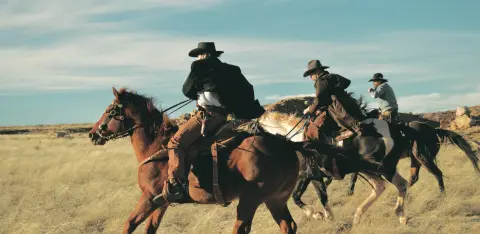 Three cowboys ride horses across a grassy field.