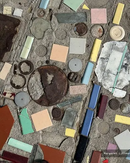 A colorful mosaic embedded into a concrete surface with various tiles and metal objects.