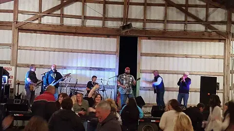 A band performs on a stage inside a barn for a crowd.