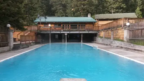 An outdoor swimming pool with a wooden building behind it, surrounded by trees.