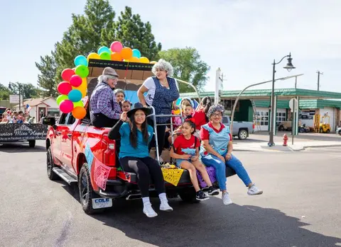 A group of people ride in the back of a red pickup truck decorated for a parade.