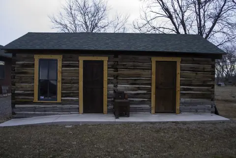 A log cabin with a green roof, a window, and two doors.