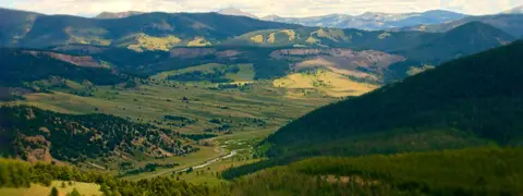 A scenic view of a vast valley surrounded by green mountains and forests.