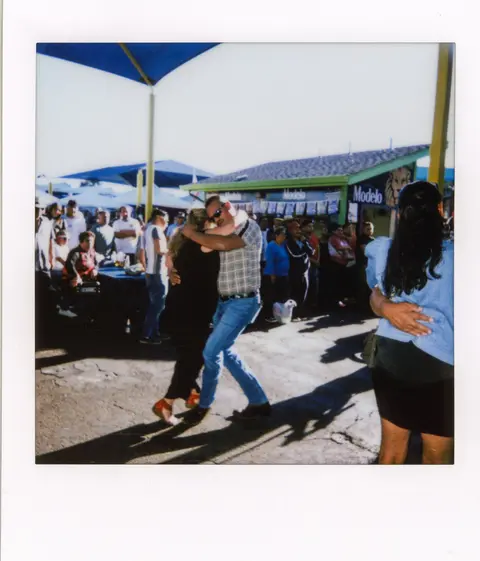 A couple dances together outdoors while a crowd looks on.