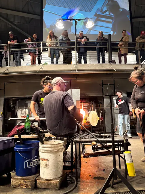 People watch glassblowers work in a studio.