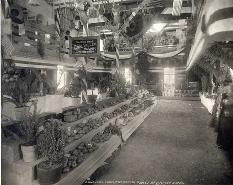 An interior view of a historic exhibition hall decorated with American flags, animal mounts, and agricultural displays.