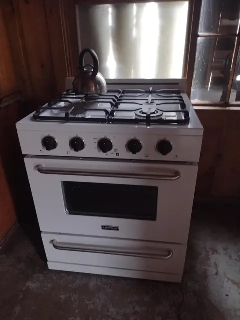 A white gas stove with a kettle on top is shown indoors.